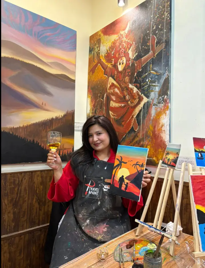 An artist in a paint-splattered apron beside vibrant canvases at the Travel & Paint studio in Kathmandu