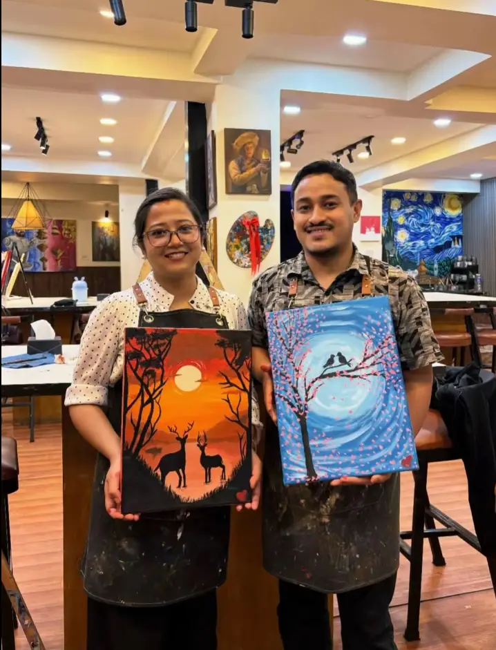 A pair holding African sunset and blue mountain landscape paintings