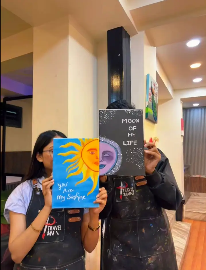 A couple holding their sun-and-moon canvas paintings on a date night in Kathmandu