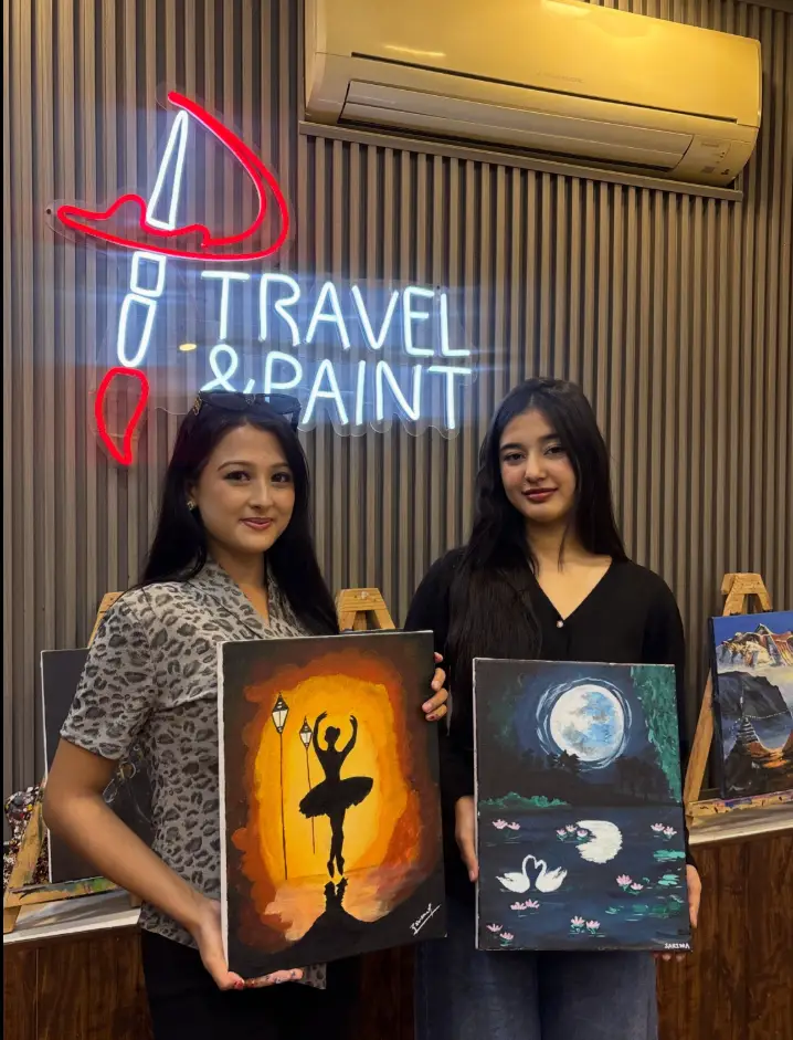 Two friends holding ballerina and moonlit paintings at the sip and paint studio