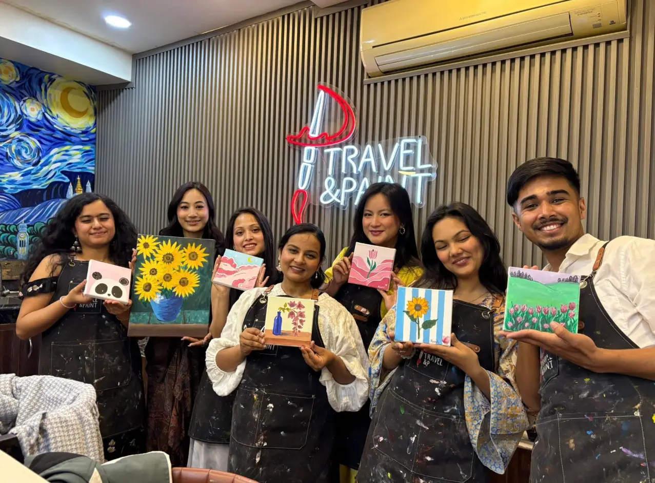 A joyful group holding canvases under the Travel & Paint neon sign in Kathmandu