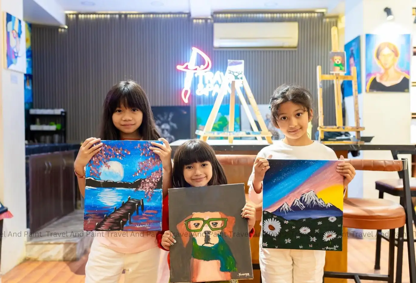Three children holding their finished acrylic paintings at the Travel & Paint studio in Kathmandu